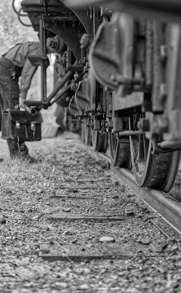 Nachrichtenarchiv – News Snaps Black and white photograph of a vintage train and engineer performing maintenance on railway tracks.